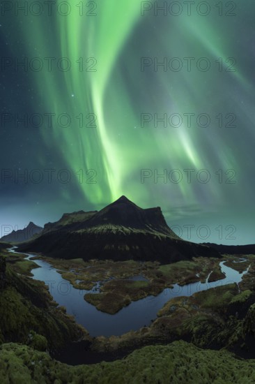 Vivid green Northern Lights dance in the sky above the dark silhouette of Iceland's rugged mountain terrain and reflective water