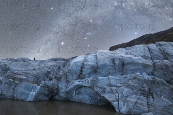 A lone figure stands atop a majestic glacier in Iceland The night sky is filled with a breathtaking display of stars, capturing the ethereal beauty of the northern nights
