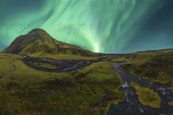 Majestic Northern Lights dance in the sky above a vibrant green valley in Iceland, with a meandering river reflecting the auroral display