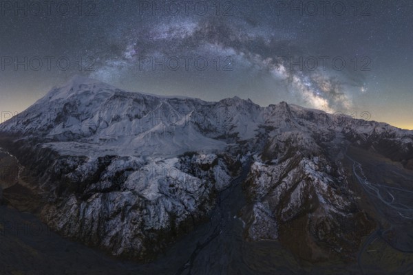 Stunning view of Icelandic mountains blanketed in snow, illuminated by a dazzling starry night sky The Milky Way arches above, showcasing nature's serene beauty