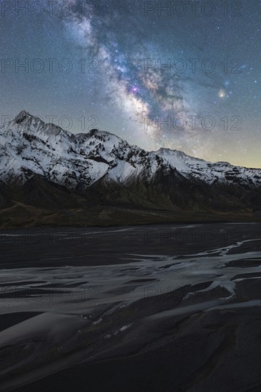 A stunning view of the Milky Way illuminating the serene, icy landscape of Iceland Snow-capped mountains and a tranquil riverbed complete this breathtaking scene