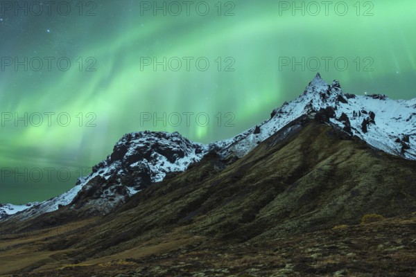 A mesmerizing northern light display dances above snow-capped mountains under a starry Icelandic sky