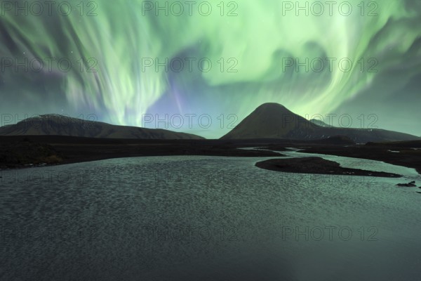 Majestic Northern Lights (Aurora Borealis) illuminate the night sky above a serene Icelandic lake, with vivid green hues reflecting in the water against a backdrop of mountains