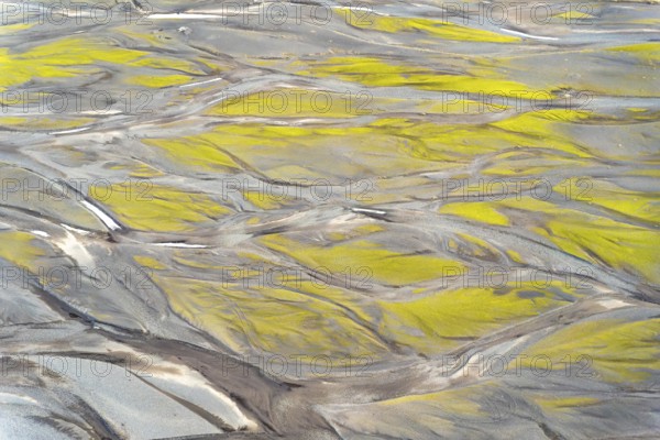 Aerial view showcasing intricate textures and patterns created by vibrant Icelandic rivers. Natural earthy tones merge with bright green hues, depicting a breathtaking landscape