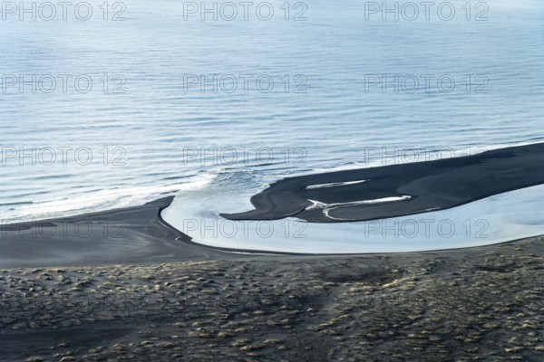 Aerial view of a winding Icelandic river meeting the sea. Black sand contrasts with the blue water, creating unique patterns and textures under a soft sky