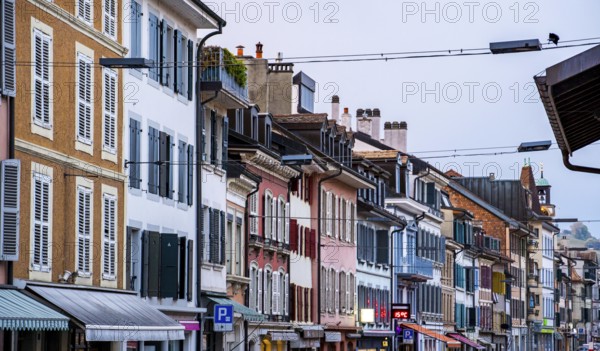 A vibrant street view of Rolle, Switzerland, showcasing colorful historic buildings with charming shutters, urban details, and a peaceful small-town atmosphere in the early evening
