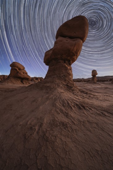 Captivating night sky with star trails above unique sandstone formations in Goblin Valley State Park, Utah. The dramatic landscape and celestial patterns create a stunning visual blend