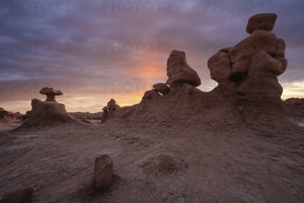 Unique sandstone formations at sunrise in Goblin Valley State Park, Utah. The sky casts a warm glow on the landscape, creating a stunning, otherworldly scene