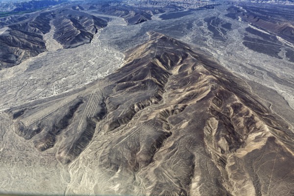 Barren desert landscape from above, distinct lines and geoglyphs visible in the mountains, the geoglyphs and images in the desert near Nasca and Palpa in Peru