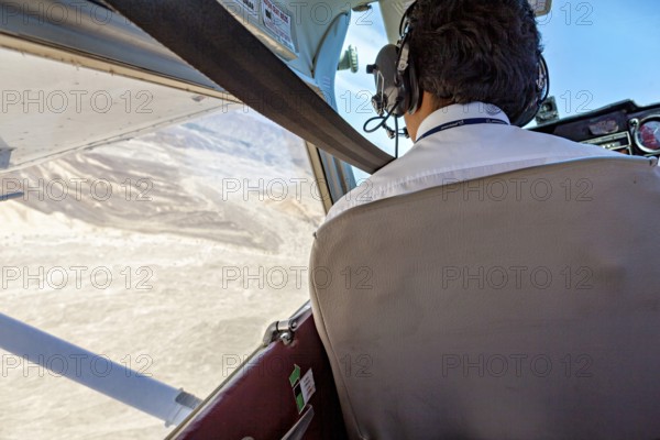 View from the cockpit of an airplane with a pilot and landscape in the background, pilot in a light aircraft above the Nascal lines in Peru