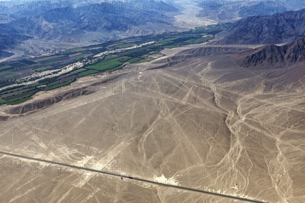 View of Nazca lines with contrasting green fields and mountain ranges in the background, the geoglyphs and paintings in the desert near Nasca and Palpa in Peru