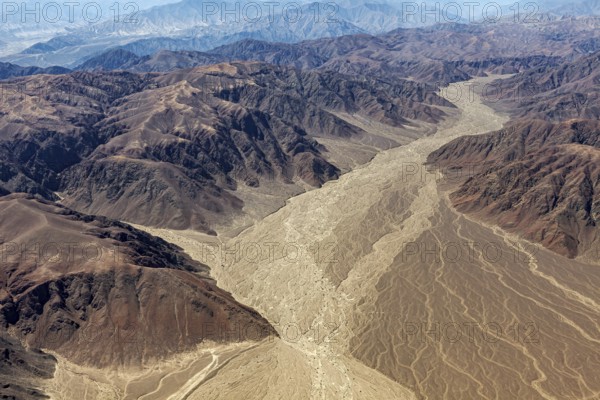 Aerial view of a dry mountain landscape with a dried-out riverbed surrounded by brown and ochre-colored mountains, The desert landscape near Nasca in Peru