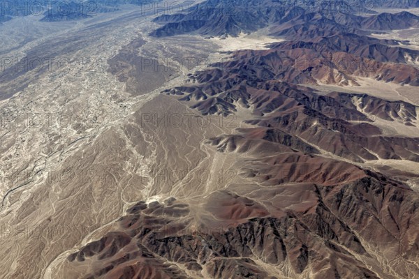 Extensive desert landscape and mountains with many shades of brown and ochre, a dried-out riverbed runs through the scene, The desert landscape near Nasca in Peru