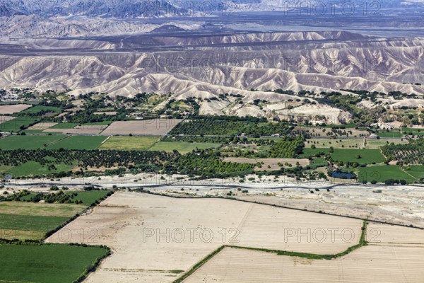 Extensive green areas and riverbed with mountain ranges on the horizon, the desert landscape near Nasca in Peru