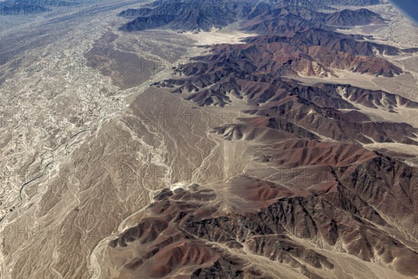 A rugged desert landscape with a series of mountains and a dried-out riverbed, brown and earthy tones dominate, The desert landscape near Nasca in Peru