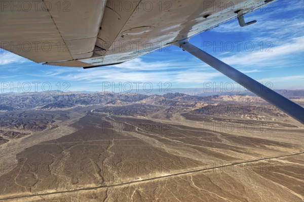 View from an airplane over desert and mountains under a blue sky, the desert landscape near Nasca in Peru