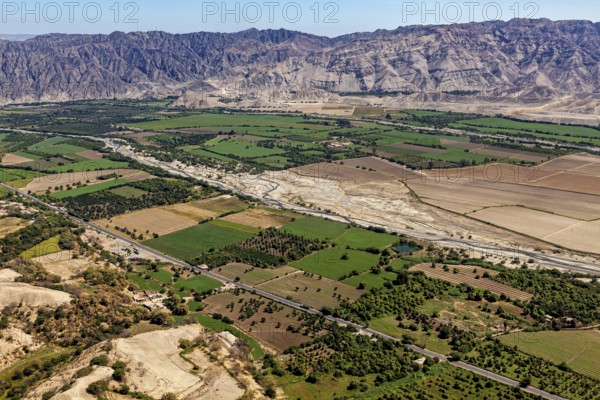 Green fields and river valley in front of a rocky mountain range under clear sky, the desert landscape near Nasca in Peru
