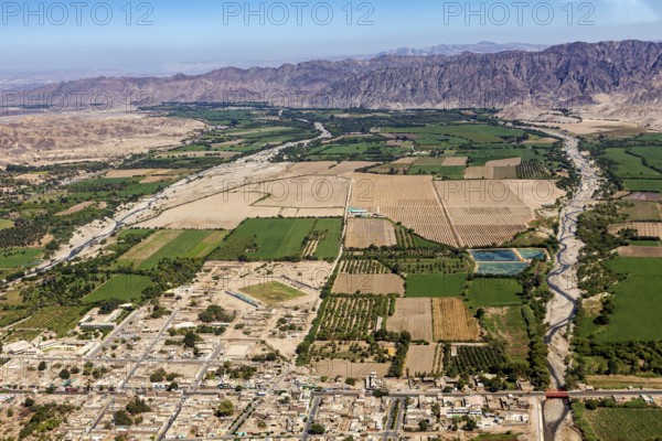 View of fields and cityscape along a river and mountains in the background, The desert landscape near Nasca in Peru