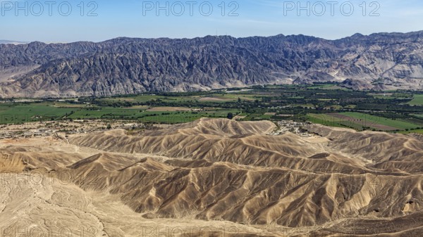 Contrasting landscape with desert in the foreground and green fields in front of a mountain chain, The desert landscape near Nasca in Peru