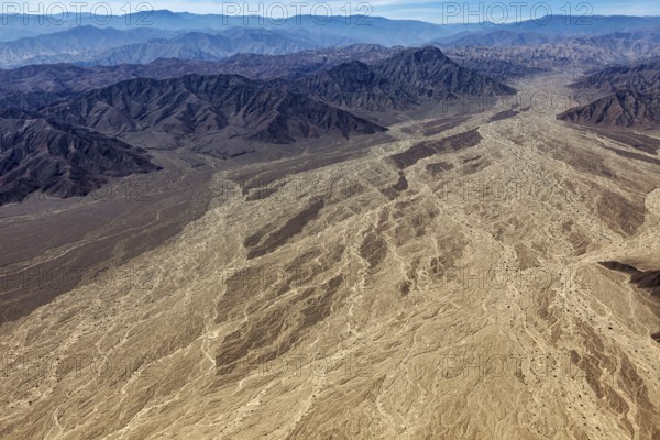 Large-scale desert landscape with a complex pattern of dry river beds surrounded by a mountain range under clear skies, The desert landscape near Nasca in Peru