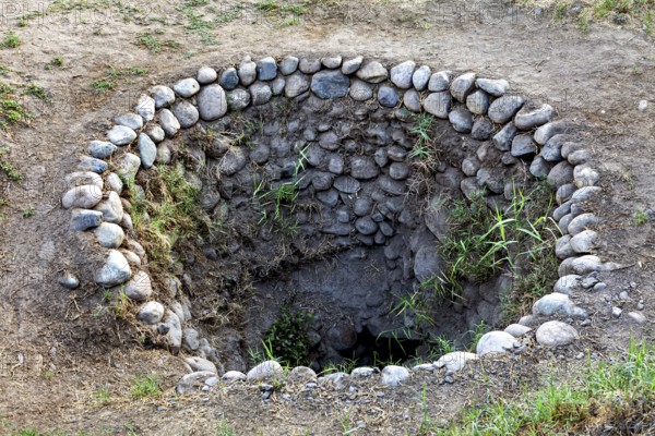 Circular hole in the ground with a rim of stones and some vegetation, The ancient Nazca wells (puquios) near Nazca, Peru