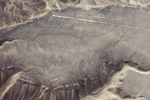 A pictogram surrounded by geoglyph lines in a sandy desert area, viewed from the air with surrounding mountains, the geoglyphs and images in the desert near Nasca and Palpa in Peru