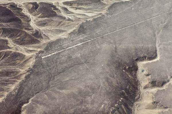 Geoglyph lines in an extensive, sand-colored desert landscape with nearby mountains, the geoglyphs and images in the desert near Nasca and Palpa in Peru