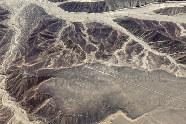 Aerial view of a mountainous desert landscape with visible eroded patterns next to Nazca lines, the geoglyphs and images in the desert near Nasca and Palpa in Peru
