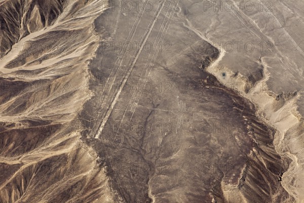 Aerial view of lines and geoglyphs in a sandy desert landscape with adjacent mountains, the geoglyphs and images in the desert near Nasca and Palpa in Peru