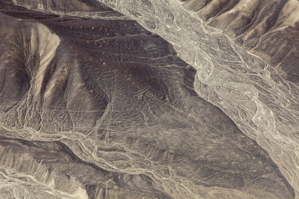 Detailed geoglyphs on a desert plain with adjacent mountain range, the geoglyphs and images in the desert near Nasca and Palpa in Peru