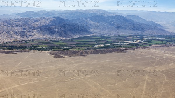 An aerial view of a desert landscape with a green oasis and mountains in the background, The landscape and desert near Nasca in the Andes of Peru