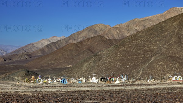 Cemetery in a desert-like landscape in front of a mountain range under clear skies, cemetery in the Nazca desert in Peru