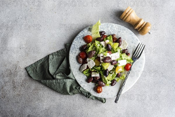 A vibrant Greek salad featuring tomatoes, lettuce, red fermented olives, and feta cheese, drizzled with oil