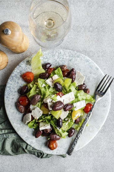 A vibrant Greek salad featuring fresh tomatoes, crisp lettuce, red fermented olives, and creamy feta cheese, paired with a glass of chilled white wine