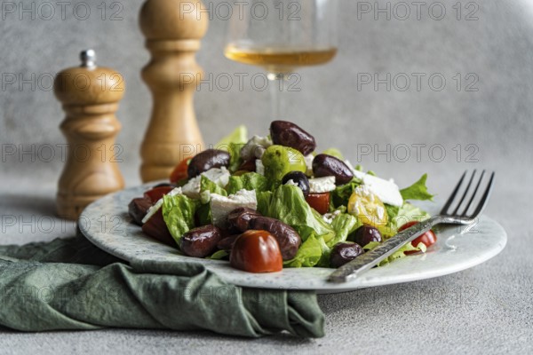 A vibrant Greek salad featuring tomatoes, lettuce, red olives, feta cheese, and olive oil A glass of cold white wine complements the healthy meal
