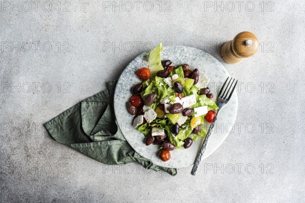 A vibrant Greek salad featuring tomatoes, lettuce, red olives, olive oil, and feta cheese Accompanied by a pepper shaker