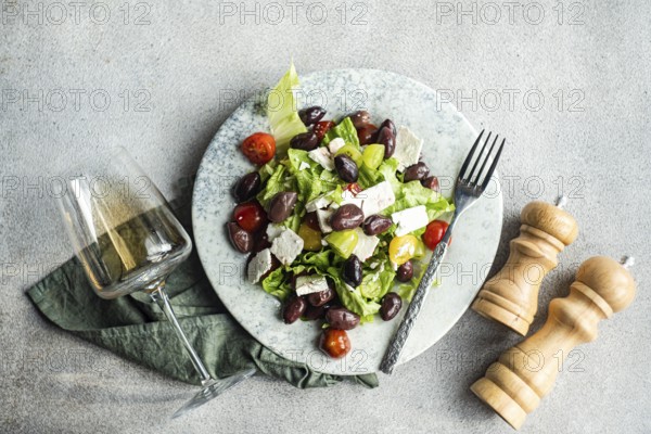 A vibrant Greek salad featuring juicy tomatoes, crisp lettuce, feta cheese, and red olives, paired with a glass of cold white wine on a rustic table