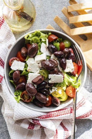 A bowl of Greek salad with tomatoes, lettuce, red fermented olives, oil, and feta cheese