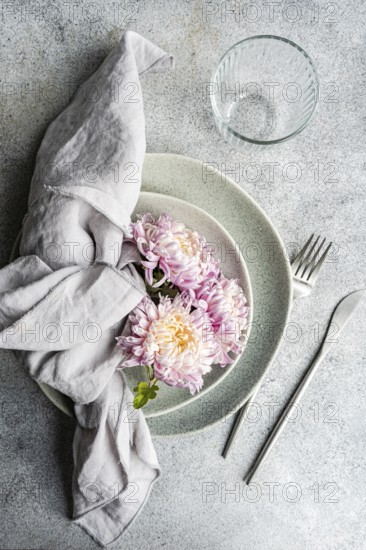 A serene table setting featuring delicate chrysanthemum flowers resting on stacked plates, accompanied by silverware The soft, neutral tones evoke a calm, autumnal feel