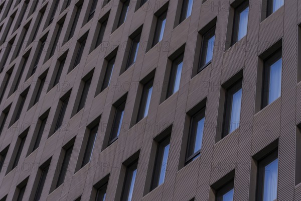 A detailed view of a modern building facade featuring a repetitive geometric pattern with aligned windows set in dark, textured cladding. This architectural design emphasizes modern aesthetics and urban style