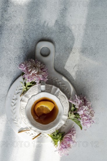 Aerial view of a rustic autumn tea setup featuring a white cup and saucer on stone, garnished with lemon slice and flanked by delicate pink chrysanthemums