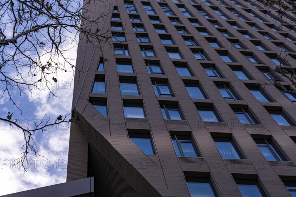 A low angle shot of a tall modern skyscraper set against a blue sky, featuring rows of windows and detailed architectural panels