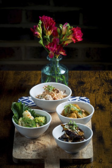 Bowls featuring chicken with glass noodles and peanuts, broccoli and cauliflower in satay sauce, tempura mushrooms in curry sauce, and aubergine stew over rice