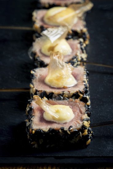 Close-up of rare tuna steaks coated in sesame seeds, topped with mayonnaise and garnished with crispy onion The elegant presentation on a black slate board highlights the gourmet and artistic dish