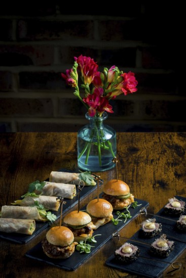 Elegant display of vegetable and courgette rolls, pulled pork and cabbage mini burgers, and rare tuna steaks with mayonnaise and seeds