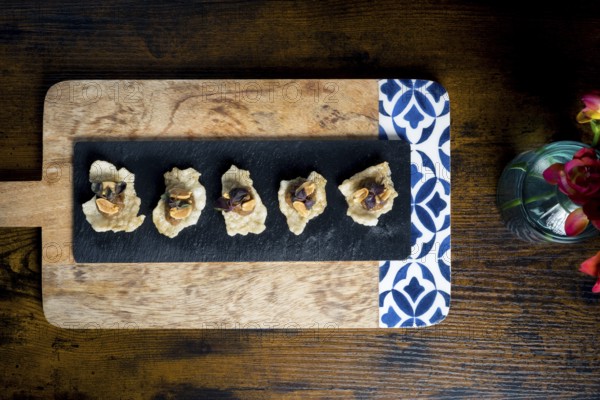 Crispy cracker canapes topped with vegetable satay stew and peanuts, arranged on a black slate over a wooden board Elegant and rustic food presentation for appetizers