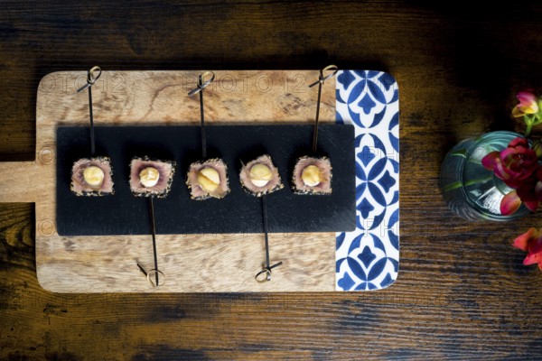 A top view of seared tuna skewers, with mayonnaise on an elegant platter The arrangement is complemented by a vibrant red flower in a vase, on a rustic wood background