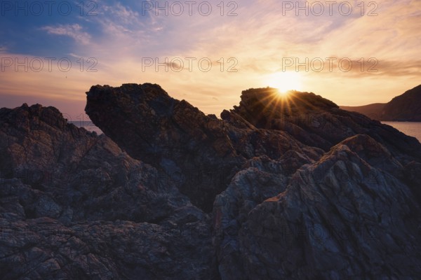 At Cala del Lastre, Portman in Murcia, Spain, a breathtaking sunset casts warm hues over rugged rocks, creating a stunning coastal view that embraces nature's beauty