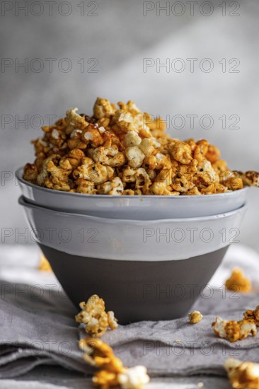 Grey bowl overflowing with sweet caramel popcorn on a textured grey cloth, showcasing a delicious snack