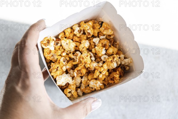 Cropped unrecognizable person in a close-up shot from above, holding a box filled with sweet caramel popcorn